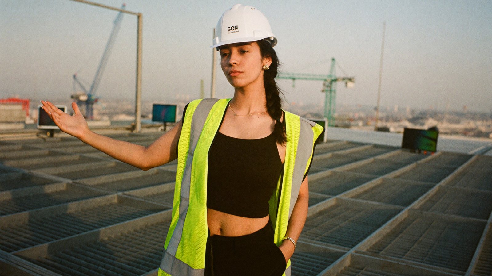 A construction company founder in a hard hat recording a vertical video on a phone on an open steel-frame floor