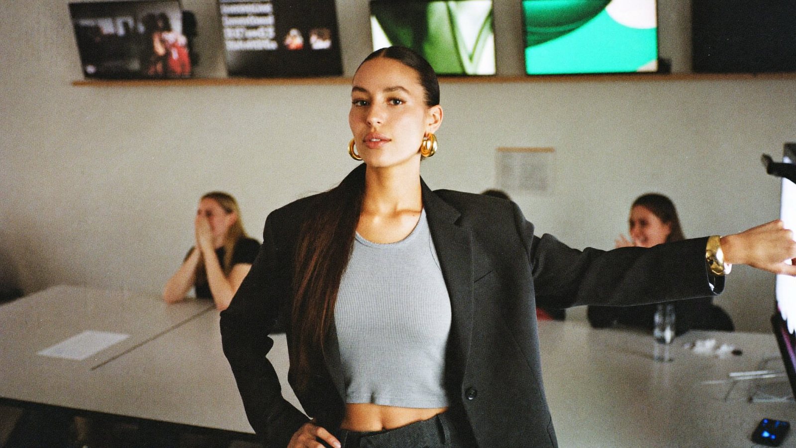 A marketing agency founder in a loft office with a wall of client campaigns, pointing at a screen while a phone on a tripod films her