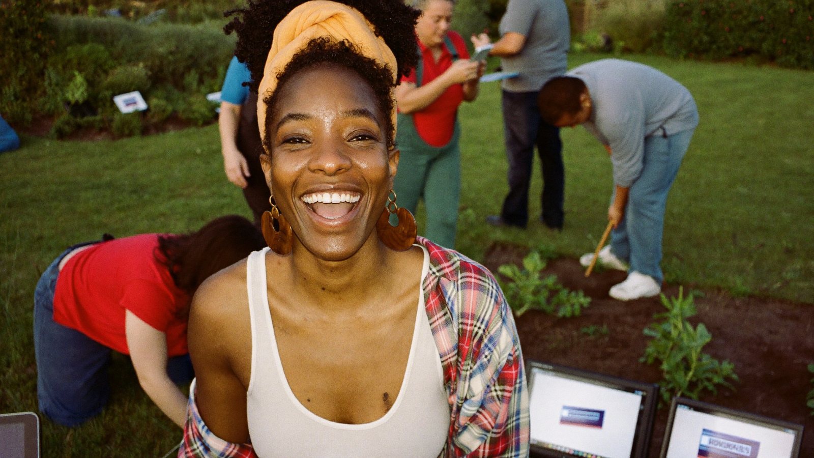 A nonprofit director recording a vertical video on a gimbal at a community garden with volunteers planting behind her