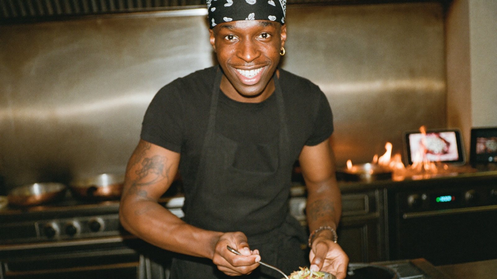 A chef-owner recording a vertical video at the pass of a busy open kitchen