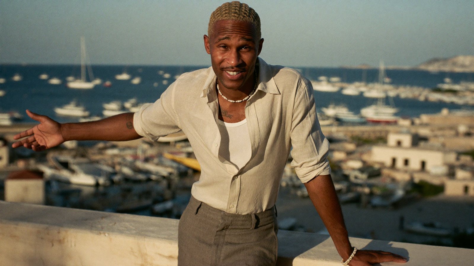 A travel advisor on a rooftop terrace over a harbour recording himself on a phone and pointing at the view